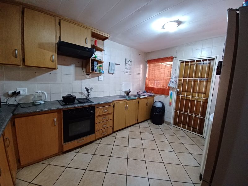 Functional kitchen featuring laminate cabinetry, built-in oven, electric hob, extractor fan, stainless steel sink, and tiled flooring with direct access to the exterior.