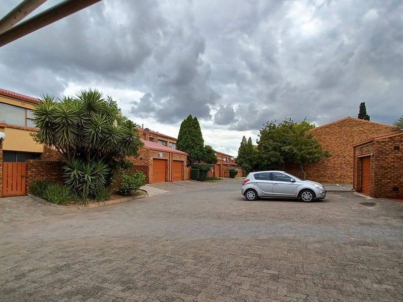 A view of the townhouse complex exterior featuring brick facades, tiled roofs, and multiple roller garage doors along a paved driveway.