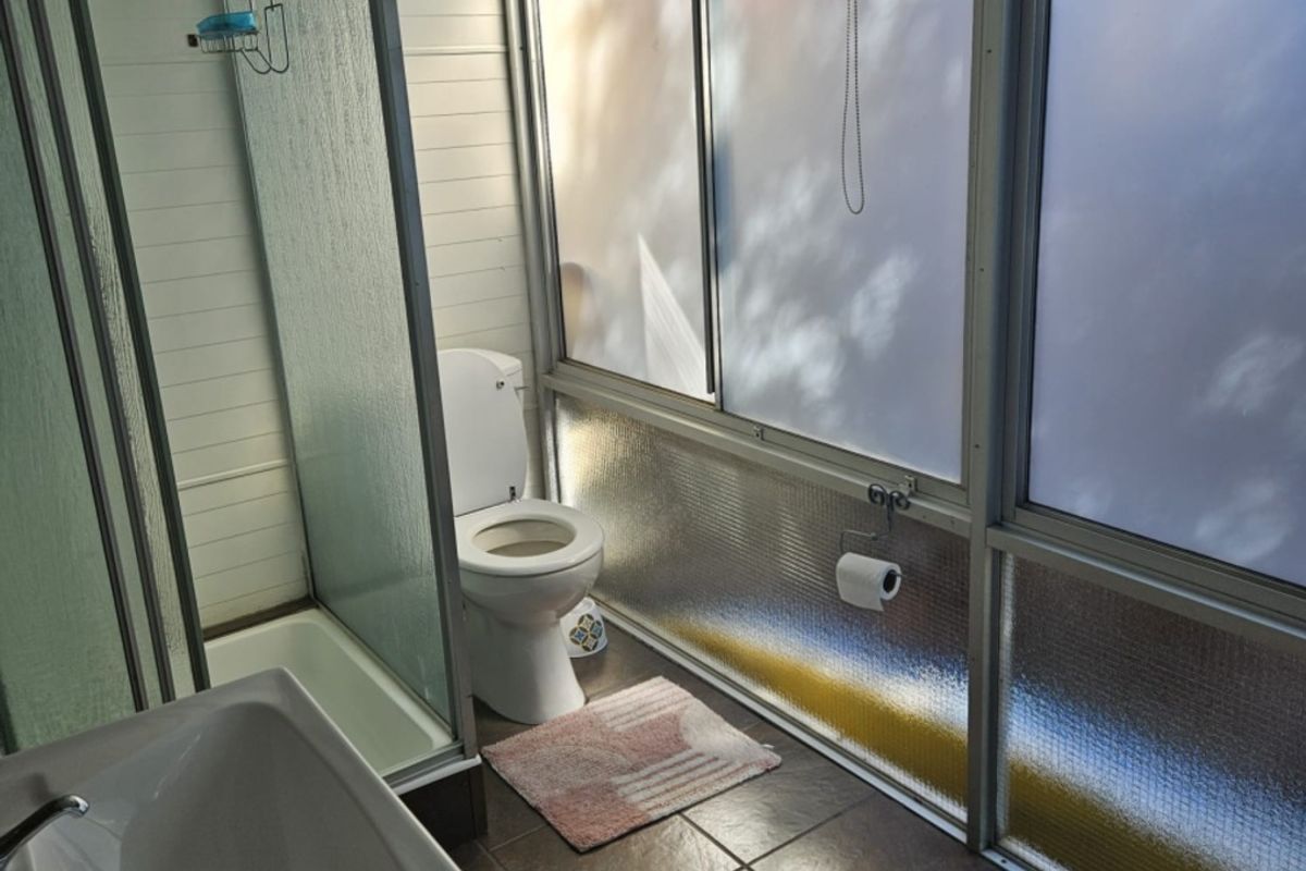 A compact bathroom featuring a shower enclosure, toilet, and pedestal sink with tiled flooring and large sliding windows.