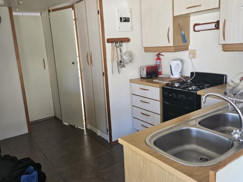 A functional kitchen featuring laminate cabinetry, a double stainless steel sink, and a gas stove with oven, set against tiled flooring.