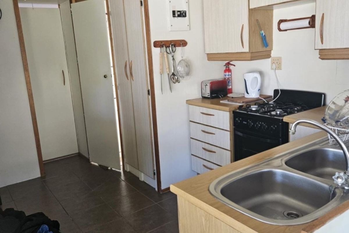 A functional kitchen featuring laminate cabinetry, a double stainless steel sink, and a gas stove with oven, set against tiled flooring.