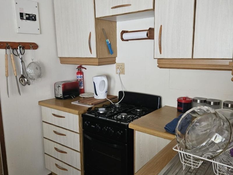 A compact kitchen featuring laminate cabinetry, wood-look countertops, a gas stove, and a stainless steel sink, providing a functional and dated workspace.