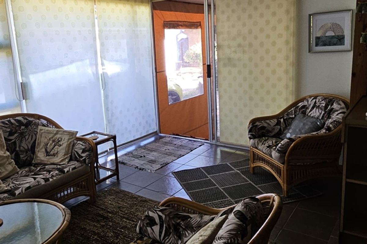 A living area featuring tiled flooring and large sliding glass doors with roller blinds, providing access to the exterior.
