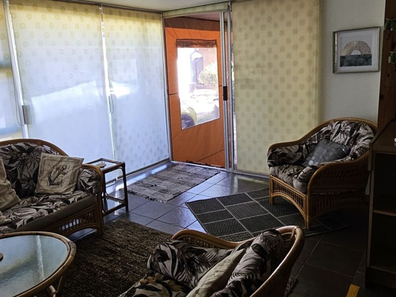 A living area featuring tiled flooring and large sliding glass doors with roller blinds, providing access to the exterior.
