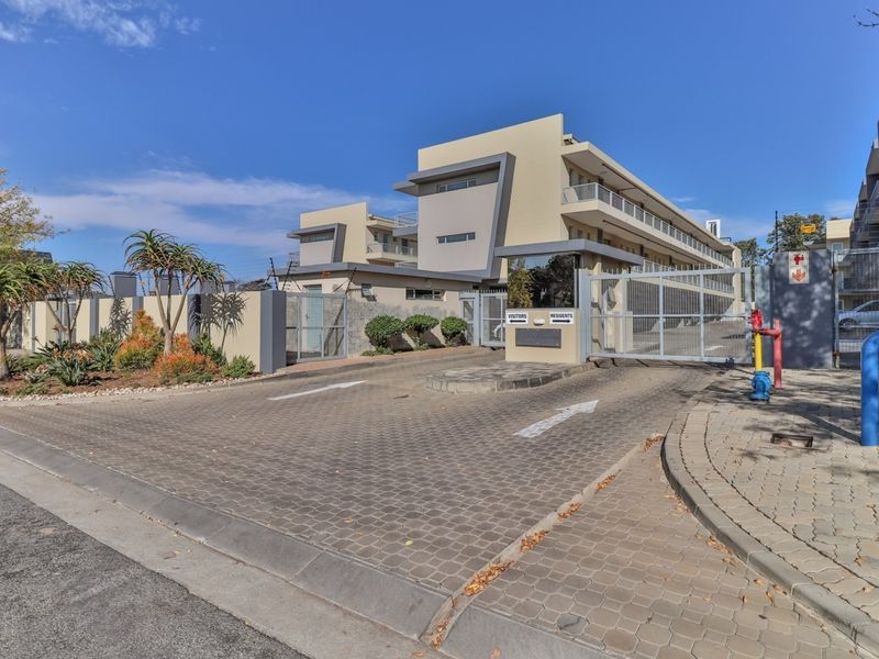 The apartment complex entrance features a paved driveway, secure gated access for residents and visitors, and perimeter security fencing.