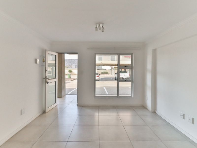 A bright, empty living area featuring neutral tiled flooring, clean white walls, and direct access to the exterior parking area.