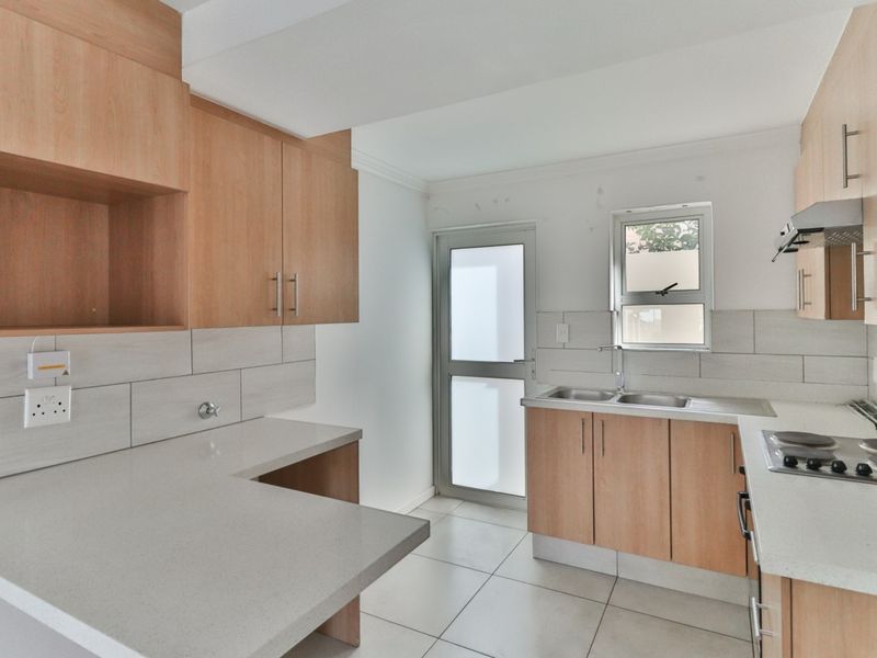 A functional kitchen featuring light wood cabinetry, stone countertops, a built-in hob with extractor, and tiled finishes throughout.