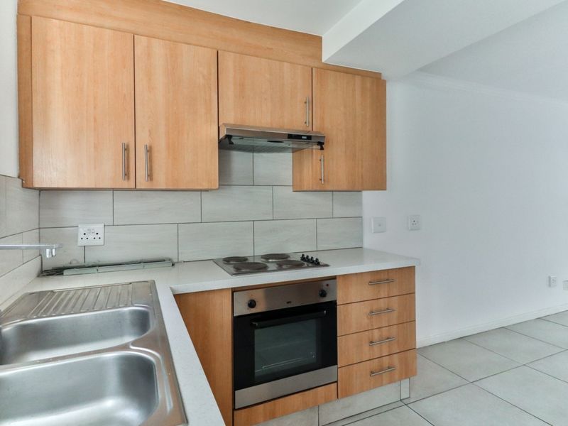 A clean, functional kitchen featuring light wood cabinetry, a built-in oven and hob, stainless steel sink, and neutral tiled backsplash.