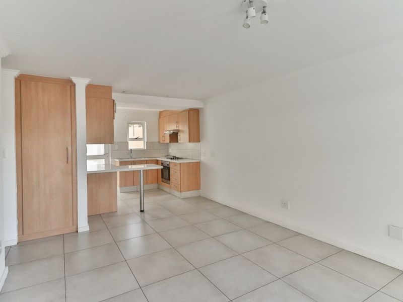 An open-plan living and kitchen area featuring light wood cabinetry, tiled flooring, and a functional breakfast counter in a clean, vacant space.