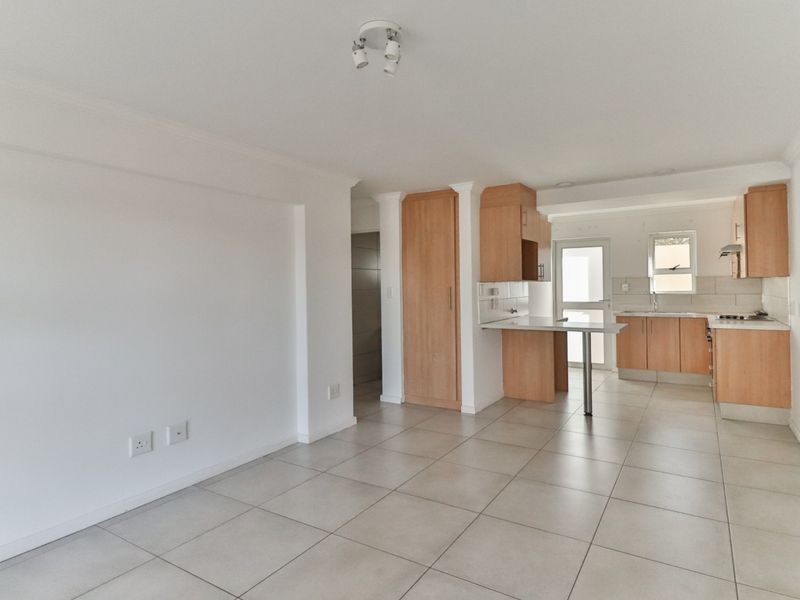 An open-plan living and kitchen area featuring tiled flooring, light wood cabinetry, a breakfast counter, and a functional kitchen layout.