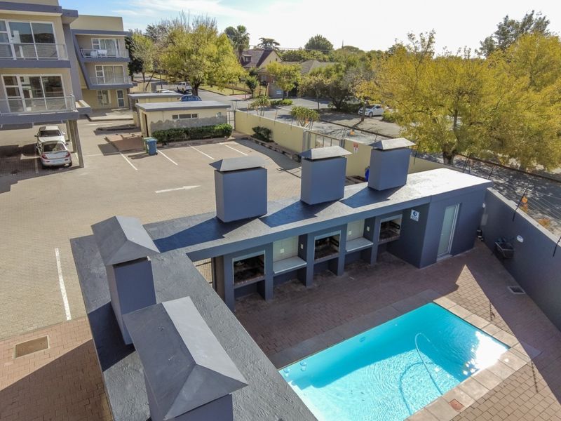 Aerial view of a communal pool area featuring multiple built-in braai stations, paved patio space, and secure perimeter walling within the apartment complex.