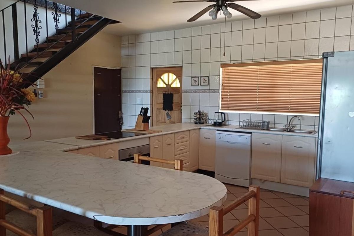 Open-plan kitchen featuring built-in cabinetry, laminate countertops, integrated oven, and a breakfast bar, adjacent to an internal staircase.