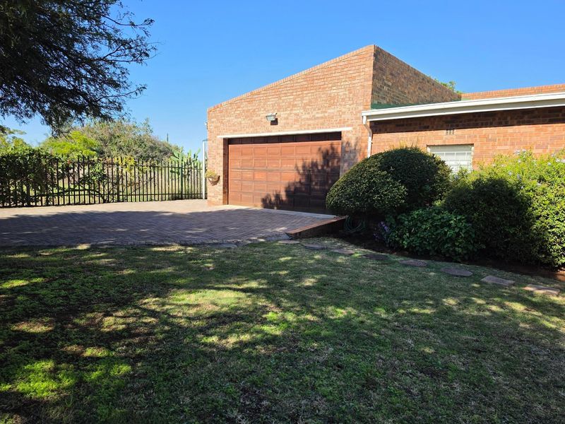 A well-maintained brick exterior featuring a paved driveway, a secure garage, and a neat front garden with established landscaping.