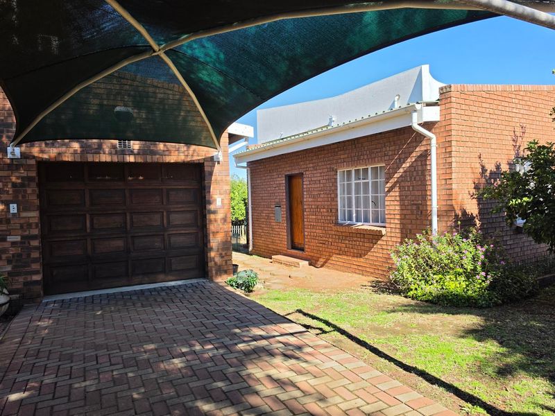 Front exterior view of a brick house featuring a paved driveway, a shade sail covered parking area, and a single garage.