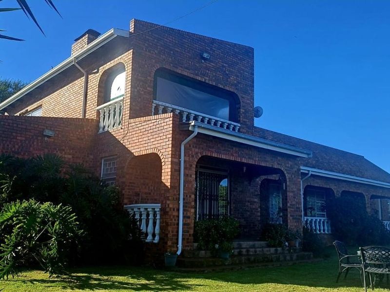 A rear view of a double-story face brick house featuring arched architectural details, a balcony with balustrades, and a well-maintained garden area.