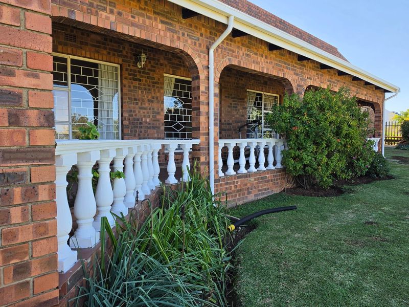 A covered patio area featuring classic face brick construction, arched architectural details, and a decorative concrete balustrade overlooking the garden.