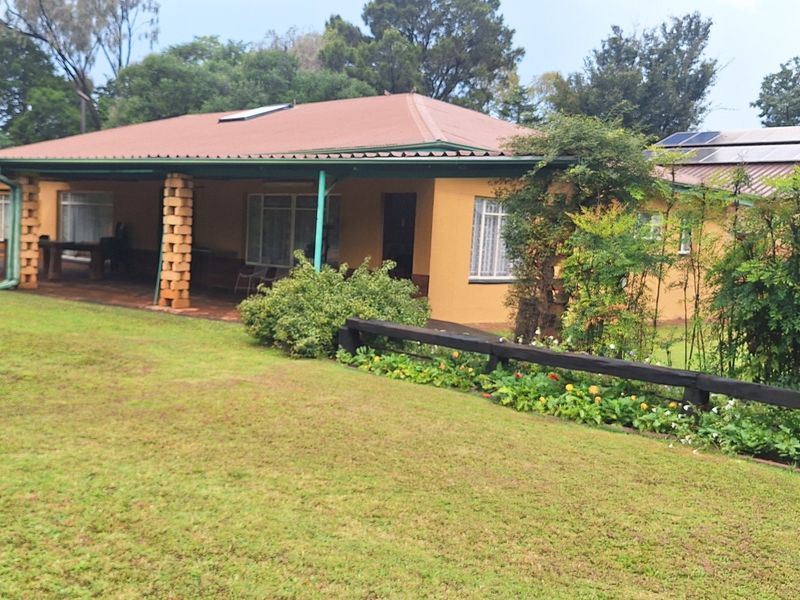 Rear view of a small holding residence featuring a covered patio with brick pillars, a metal roof, and solar panels set within a landscaped garden.