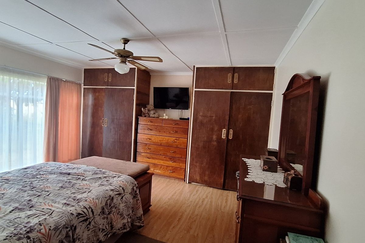 A bedroom featuring built-in wooden cupboards, laminate flooring, and a ceiling fan, with access to natural light through a sliding door.