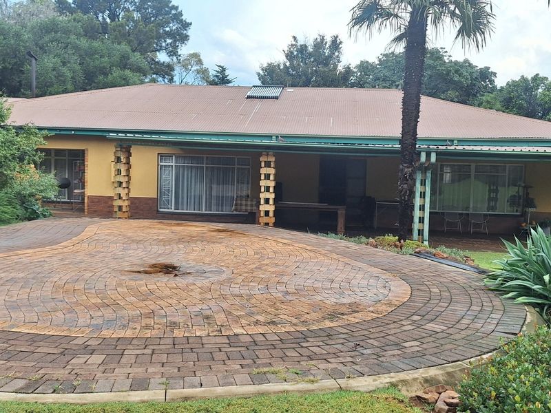 Front view of a single-story home featuring a circular paved driveway, covered patio area, and a corrugated metal roof with solar water heating.