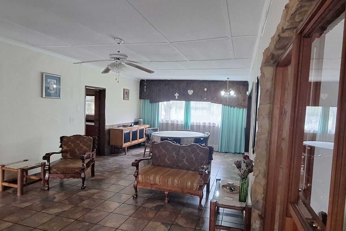 Spacious living area featuring tiled flooring, a ceiling fan, and a rustic stone feature wall, offering a comfortable and traditional layout.
