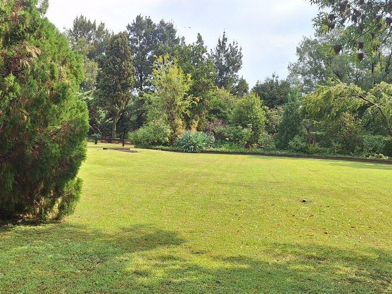 A well-maintained, expansive garden area featuring a lush green lawn surrounded by mature trees and established landscaping.