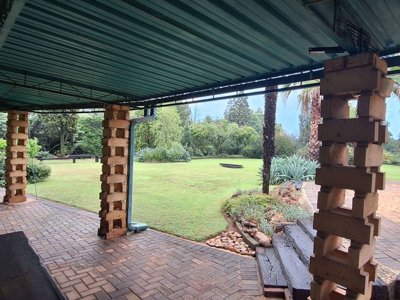 A spacious covered patio featuring brick paving and unique brick pillars, overlooking a well-maintained garden area.