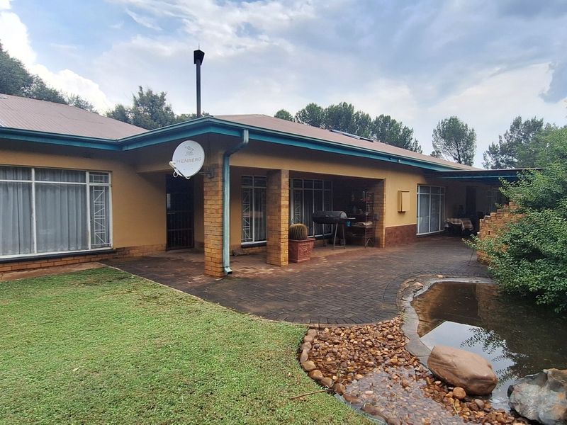 Rear view of the property featuring a covered patio, brick paved area, and a landscaped water feature set within a spacious garden.