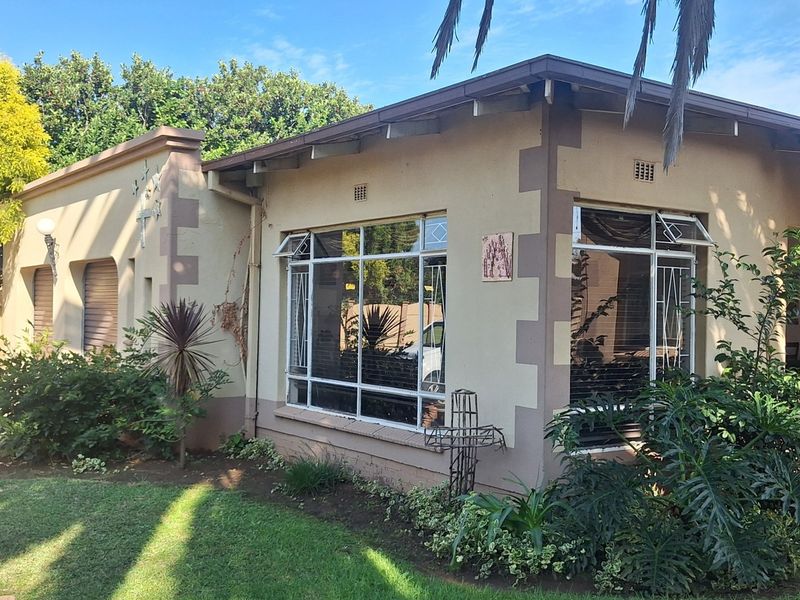 Front elevation of a single-story house featuring steel-framed windows, security bars, and a well-maintained garden area.
