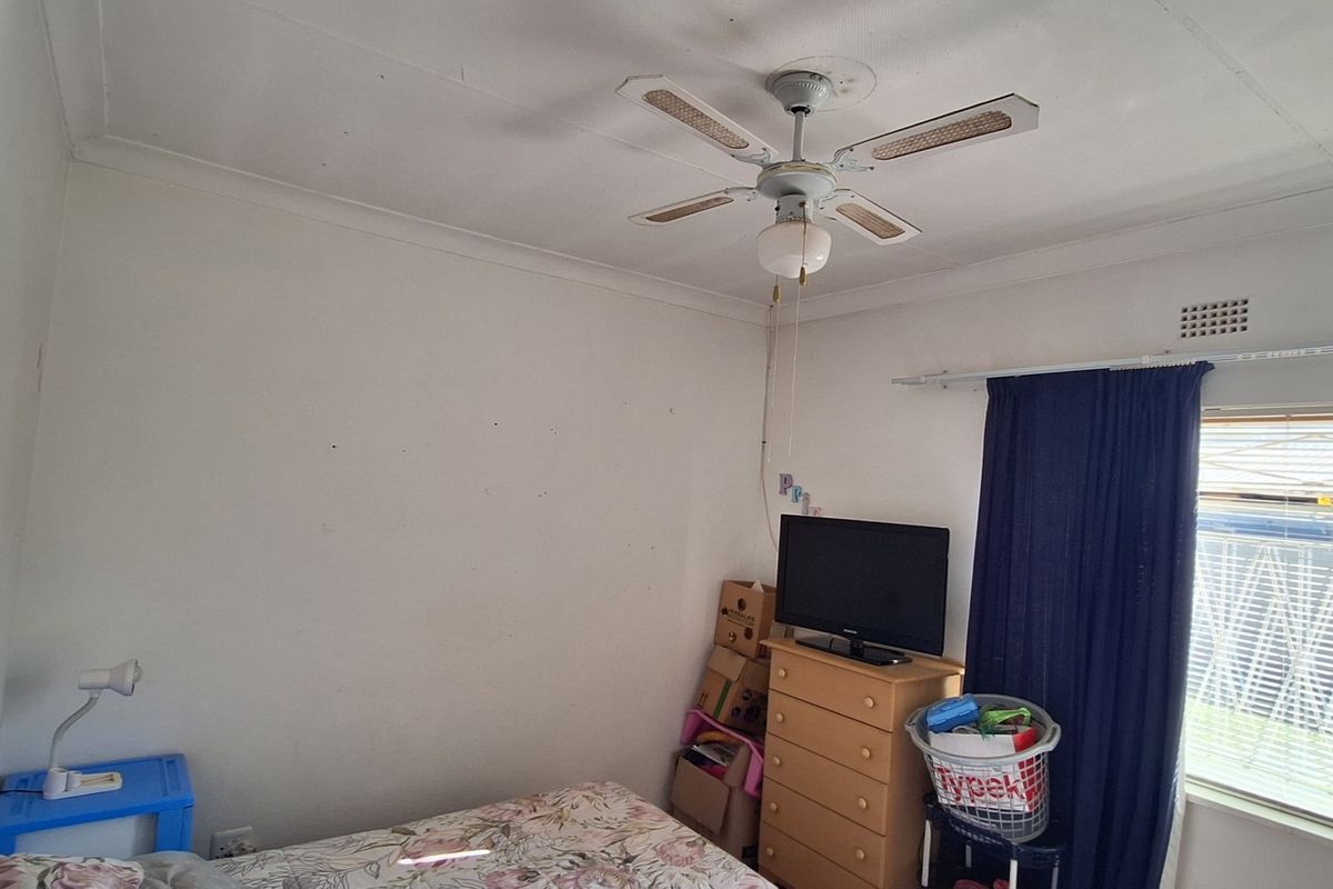 A bedroom featuring a ceiling fan, security gate on the window, and curtain rail. The room requires cosmetic updates to improve its overall condition.
