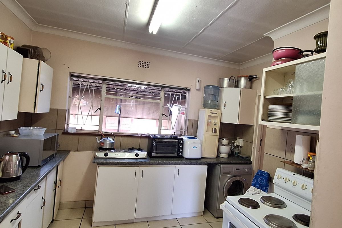A functional kitchen featuring white cabinetry, tiled backsplash, and integrated laundry plumbing, offering a practical layout with potential for modern cosmetic updates.
