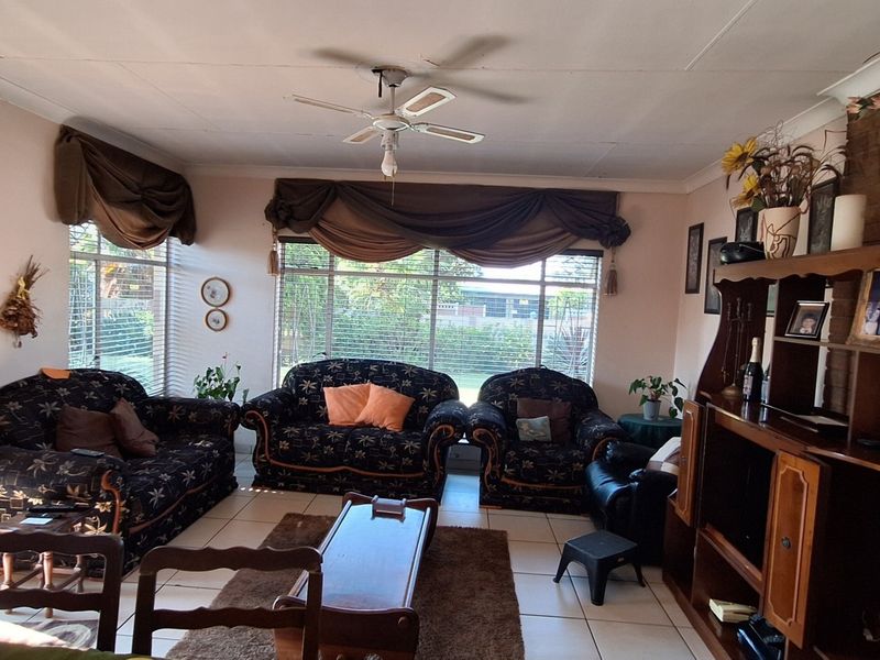 Spacious living room featuring tiled flooring, a ceiling fan, and a brick fireplace, with direct access to the garden through a sliding glass door.