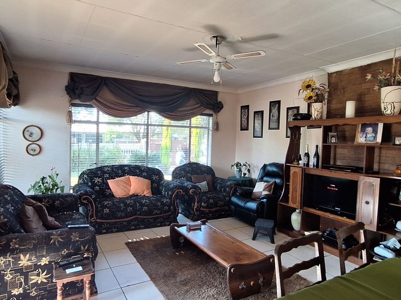 A living room featuring tiled flooring, a ceiling fan, and a brick feature wall, offering a functional space with potential for cosmetic updates.