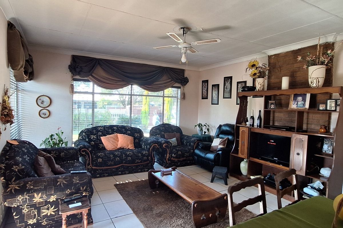 A living room featuring tiled flooring, a ceiling fan, and a brick feature wall, offering a functional space with potential for cosmetic updates.