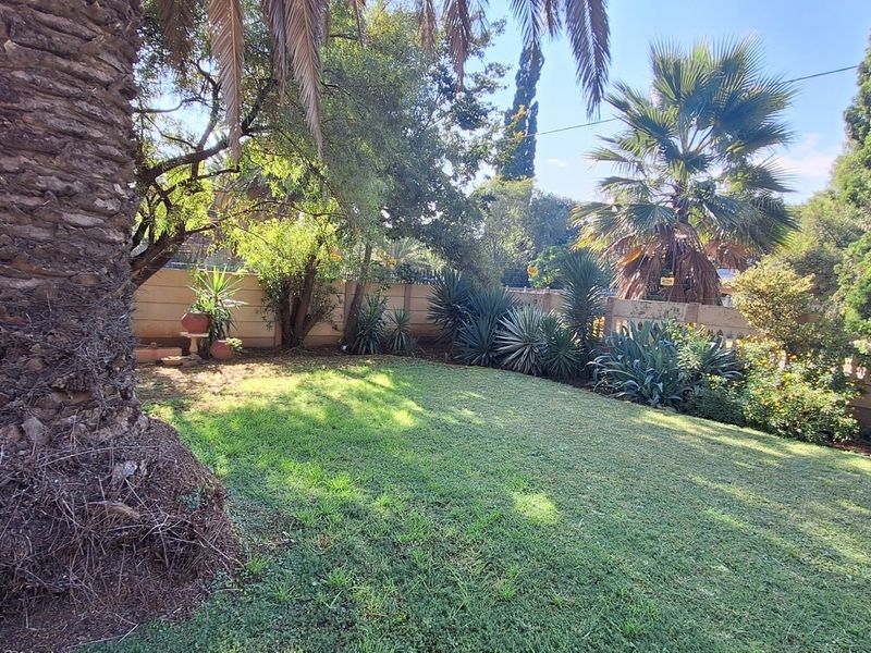 A well-maintained private garden featuring a lush lawn, mature palm trees, and established perimeter walling.