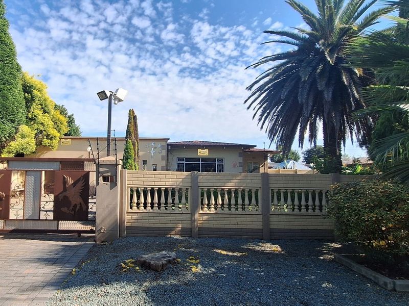 Front view of the property featuring a secure perimeter wall with balustrade detailing, electric fencing, and a decorative metal entrance gate.