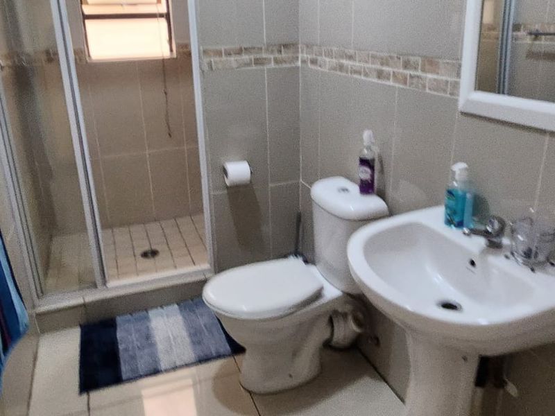 A functional bathroom featuring a shower enclosure, pedestal basin, and toilet with neutral wall and floor tiling.