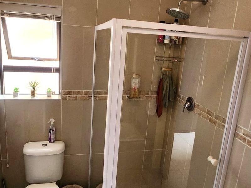A compact bathroom featuring a glass-enclosed shower, a toilet, and neutral wall tiling with a decorative border.