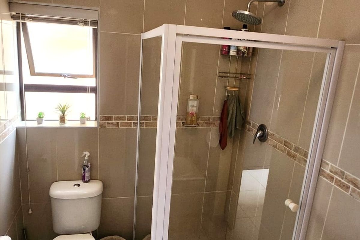 A compact bathroom featuring a glass-enclosed shower, a toilet, and neutral wall tiling with a decorative border.