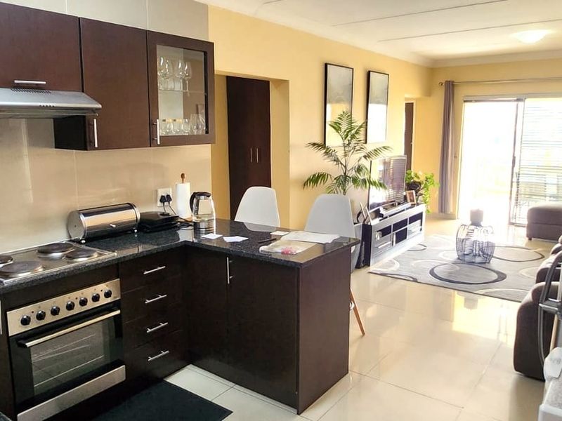 Open-plan kitchen and living area featuring dark wood cabinetry, granite countertops, integrated appliances, and tiled flooring leading to a balcony.