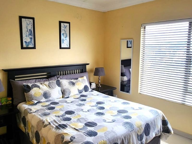 A functional bedroom featuring neutral wall tones, tiled flooring, and venetian blinds allowing for natural light.