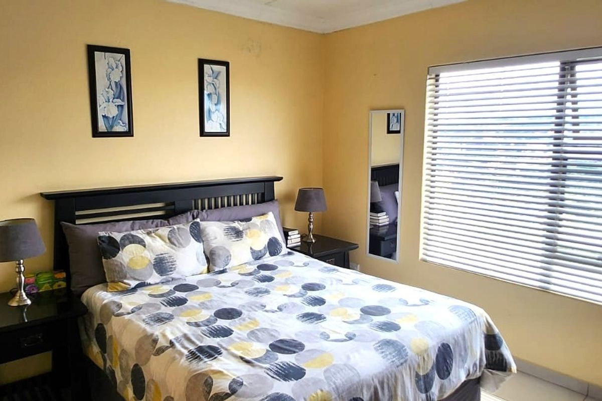 A functional bedroom featuring neutral wall tones, tiled flooring, and venetian blinds allowing for natural light.