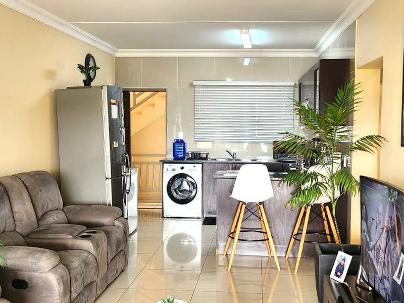 Open-plan living area featuring tiled flooring and a functional kitchen with built-in cabinetry, oven, and extractor fan.