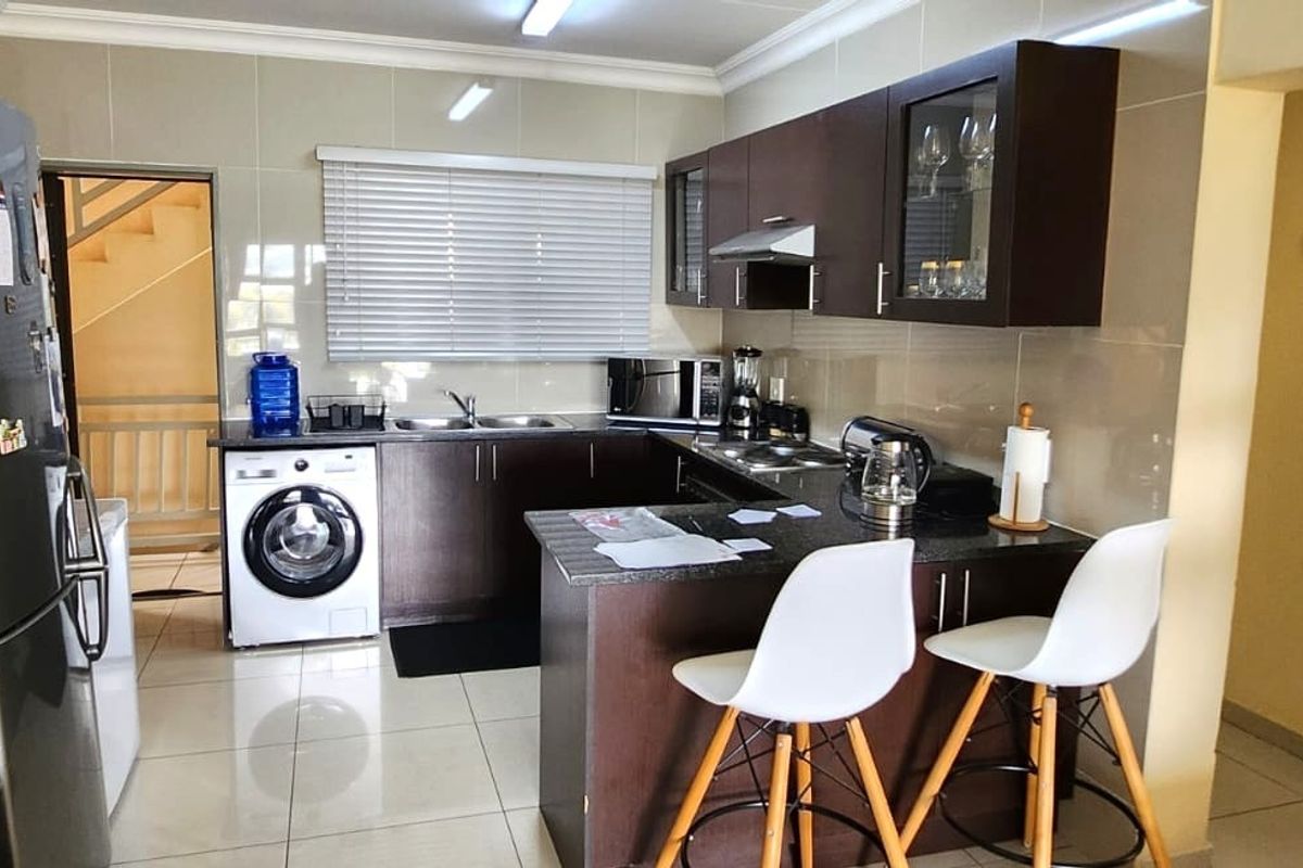 A functional kitchen featuring dark wood cabinetry, granite countertops, a double basin sink, and tiled flooring, with an integrated laundry area.