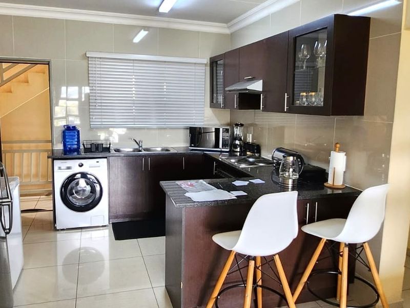 A functional kitchen featuring dark wood cabinetry, granite countertops, a double basin sink, and tiled flooring, with an integrated laundry area.