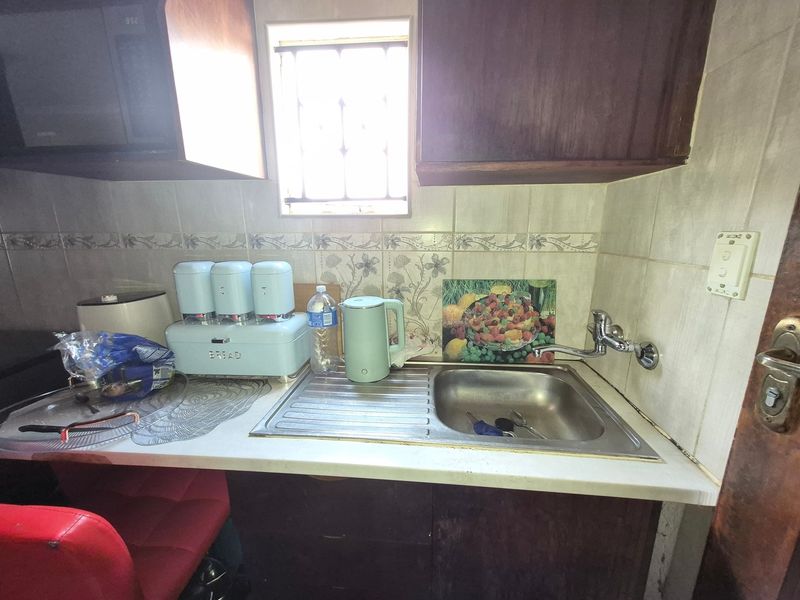 A compact kitchen area featuring built-in cabinetry, a stainless steel sink with wall-mounted faucet, and a tiled backsplash with a small window.