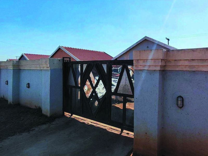 Front view of the property featuring a secure metal driveway gate and a perimeter wall with integrated exterior lighting.
