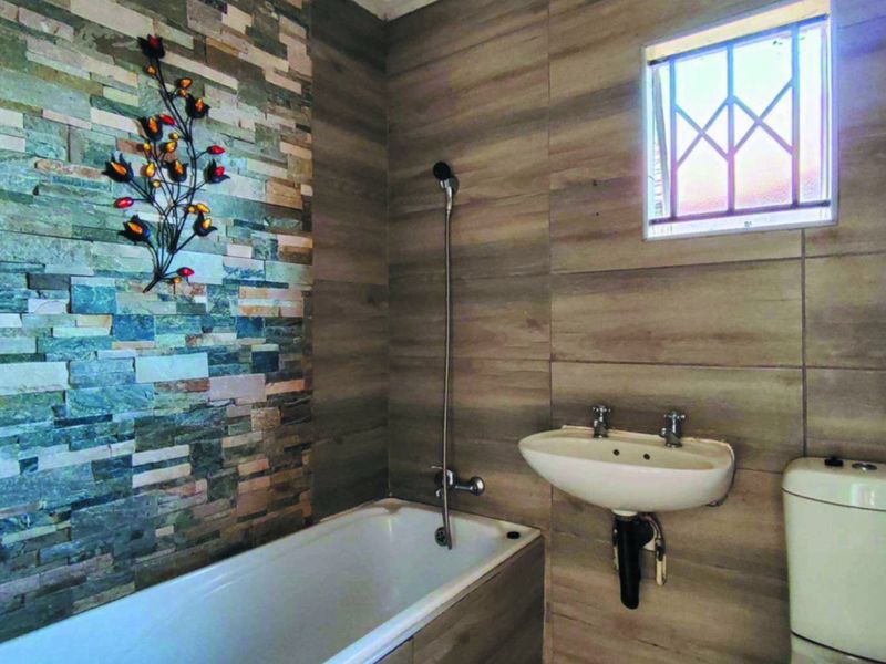 A modern bathroom featuring a stone-clad feature wall, a built-in bathtub, a wall-mounted basin, and a toilet with neutral ceramic wall tiling.