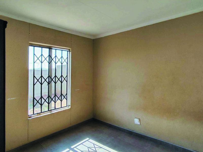 An empty bedroom featuring tiled flooring and a window fitted with a security gate, requiring cosmetic updates to the wall finishes.
