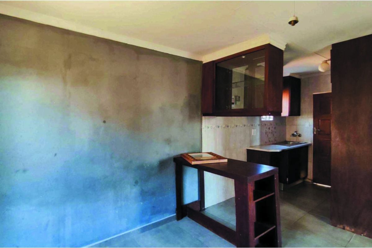 A compact kitchen area featuring built-in cabinetry, a sink, and tiled flooring, currently requiring cosmetic updates and wall finishing.