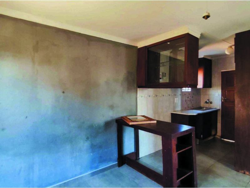 A compact kitchen area featuring built-in cabinetry, a sink, and tiled flooring, currently requiring cosmetic updates and wall finishing.